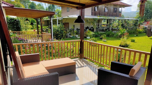 A covered outdoor seating area with wicker furniture and a view of a lush garden. - ilasan cottage (Tomohon)
