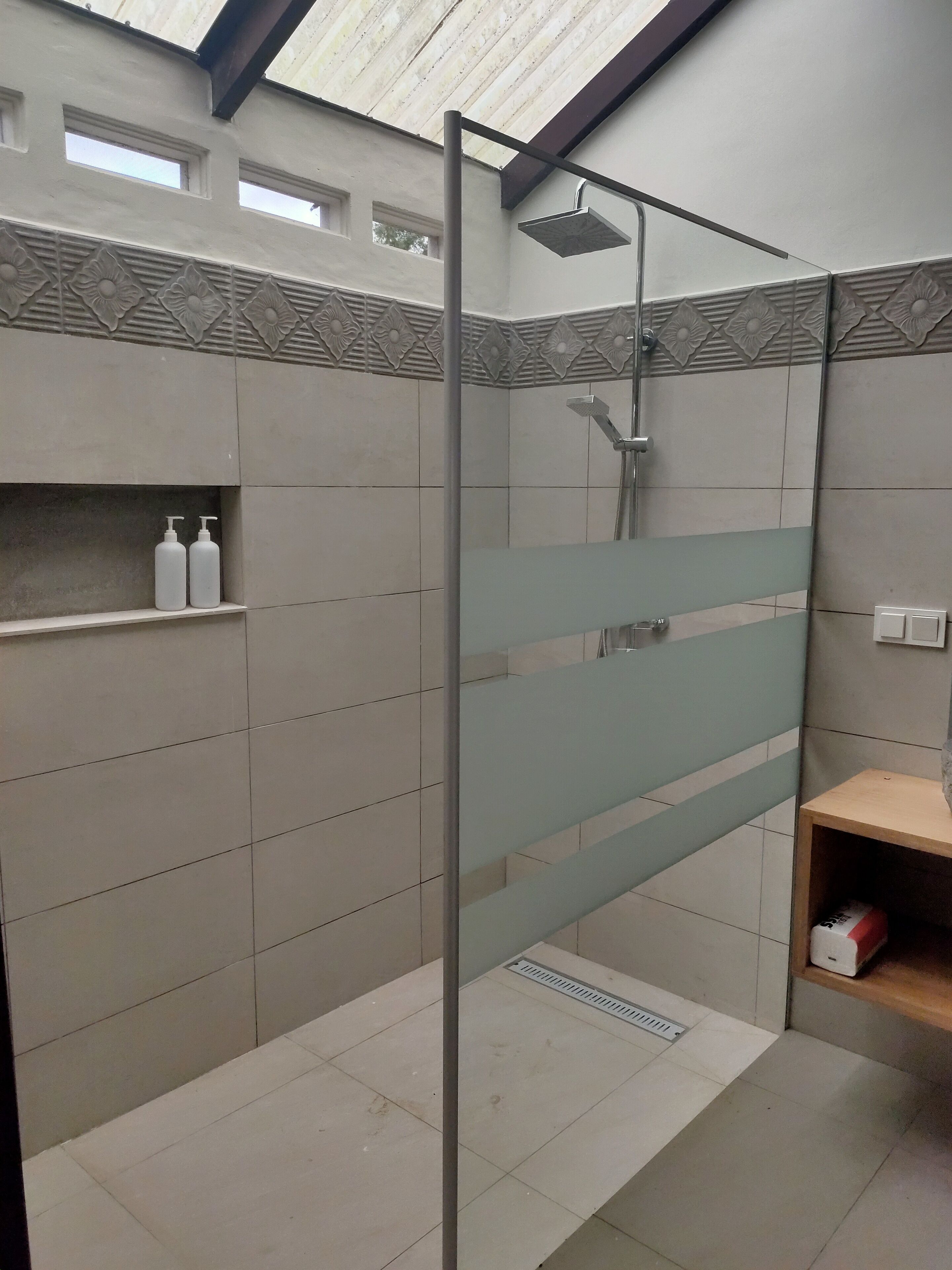 A modern bathroom with a shower, tiled walls, and a shelf with toiletries.