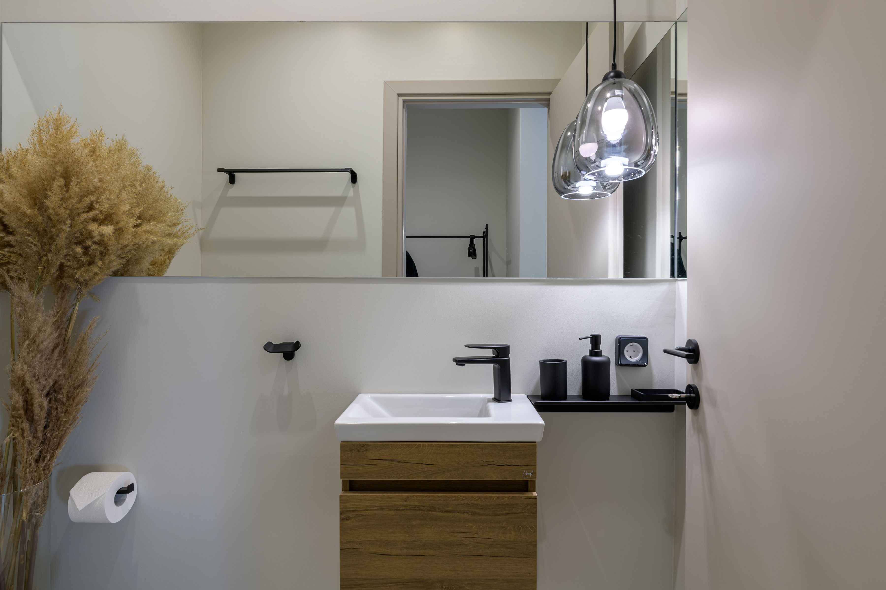 A modern bathroom with a white sink, wooden cabinet, and a mirror.