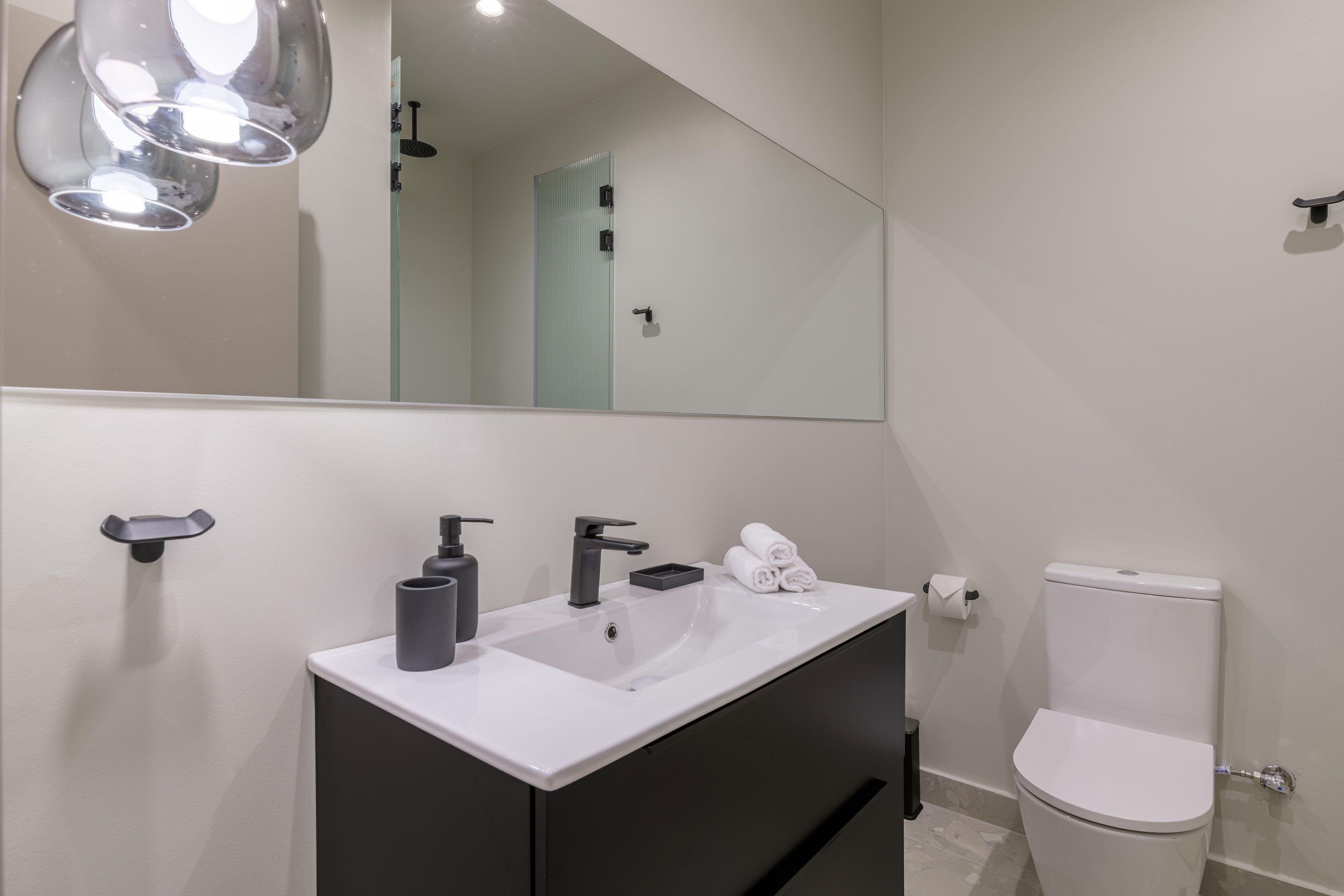 A modern bathroom with a white sink, black faucet, and a toilet.