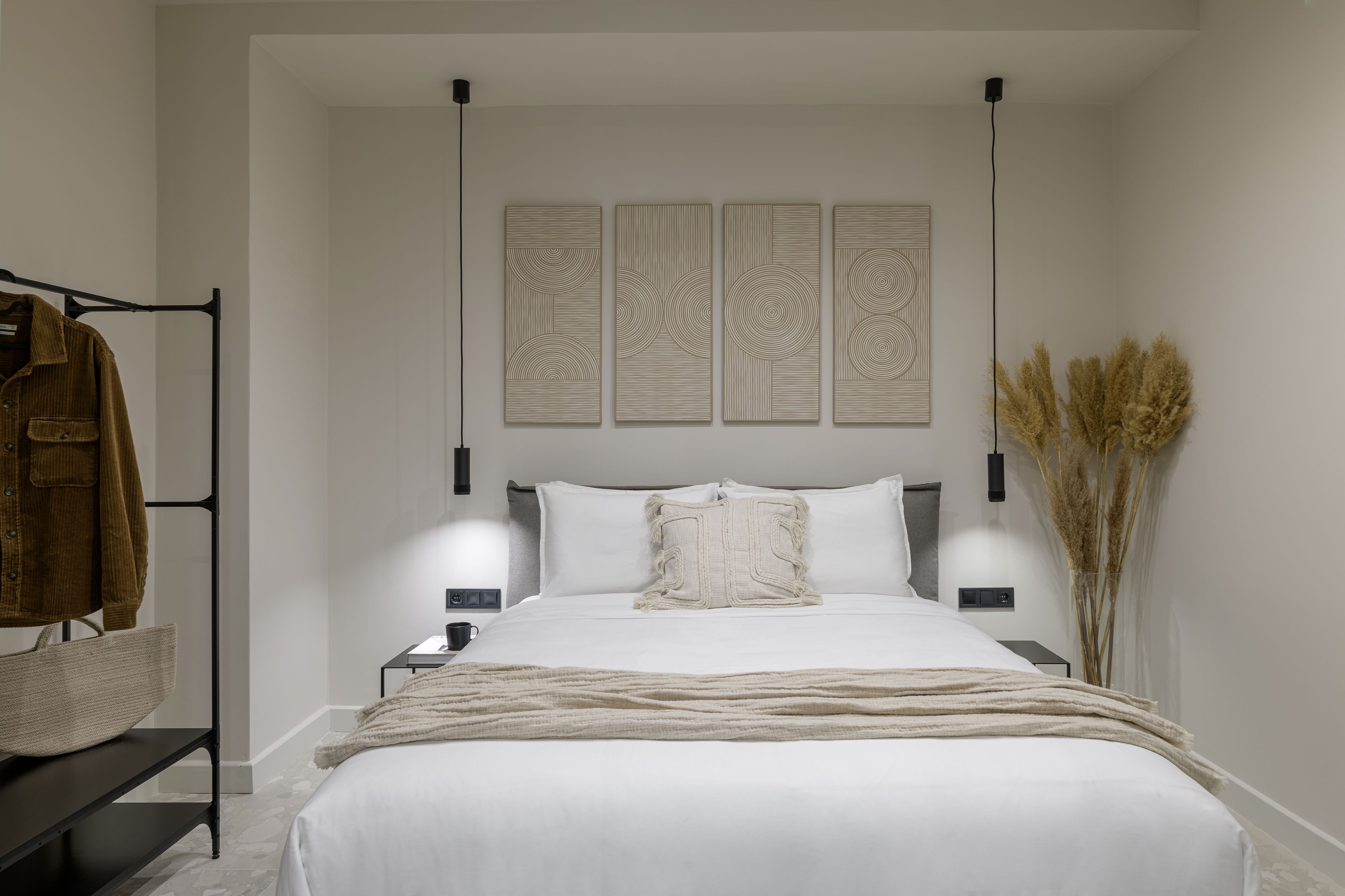 Une chambre à coucher moderne avec un grand lit, des tables de chevet, une lampe suspendue et une œuvre d’art murale.