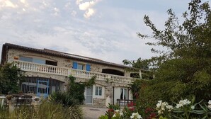 A stone building with a balcony, surrounded by greenery and flowers. - Mas "Naturelle" Cévennes (Molières-sur-Cèze)