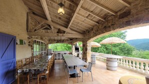 An outdoor dining area with stone walls, wooden beams, and a view of the landscape. - Mas "Naturelle" Cévennes (Molières-sur-Cèze)
