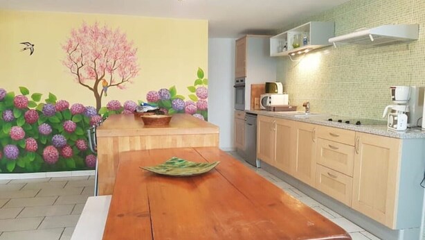 Una cocina con una mesa de madera, un mural floral en la pared y una lámpara colgante.