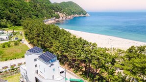 Un bâtiment situé sur la côte, doté de panneaux solaires, avec une plage et une colline boisée à proximité.