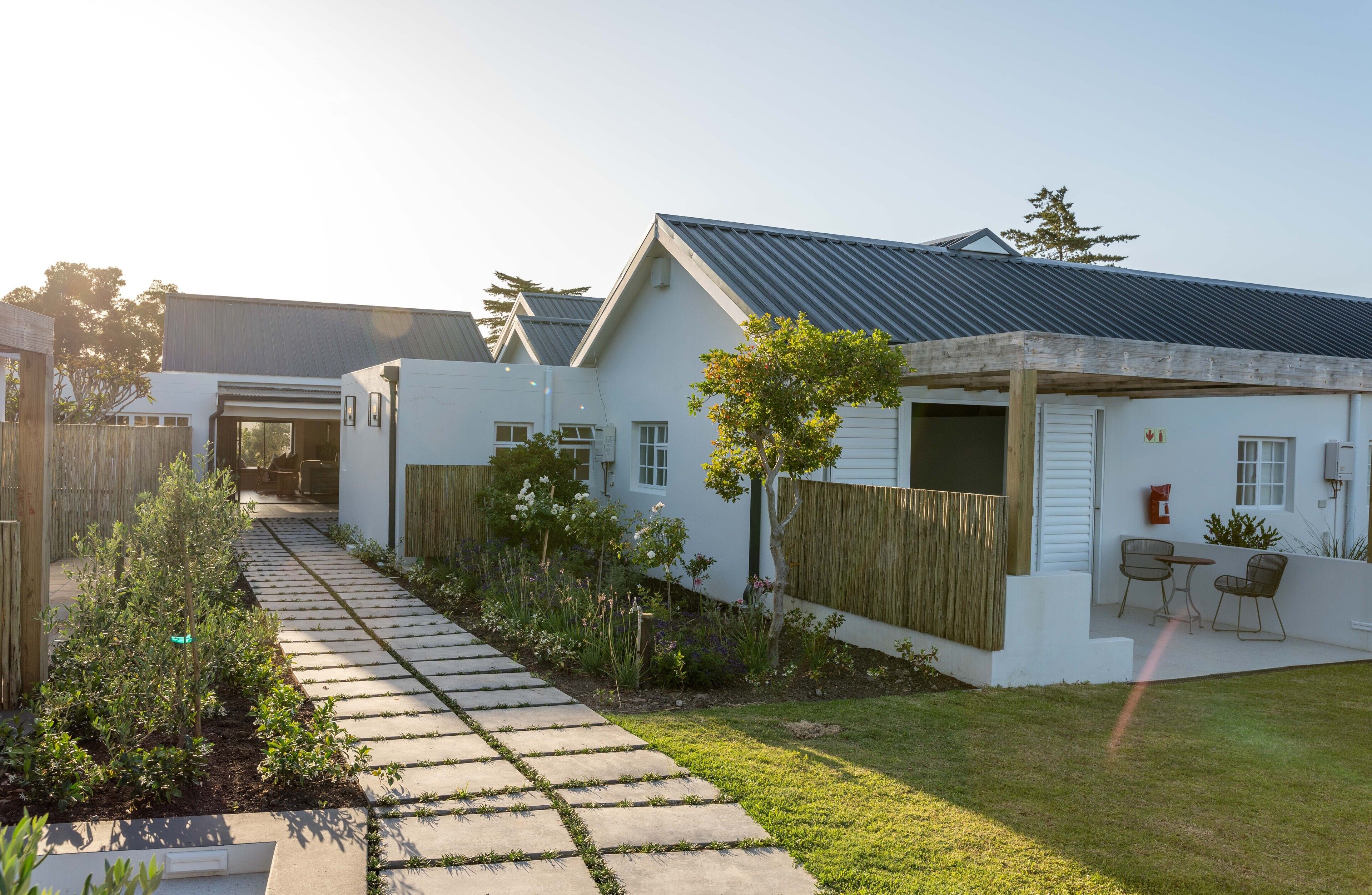 A modern house with a paved pathway leading to the entrance, surrounded by a well-maintained garden and a wooden fence.