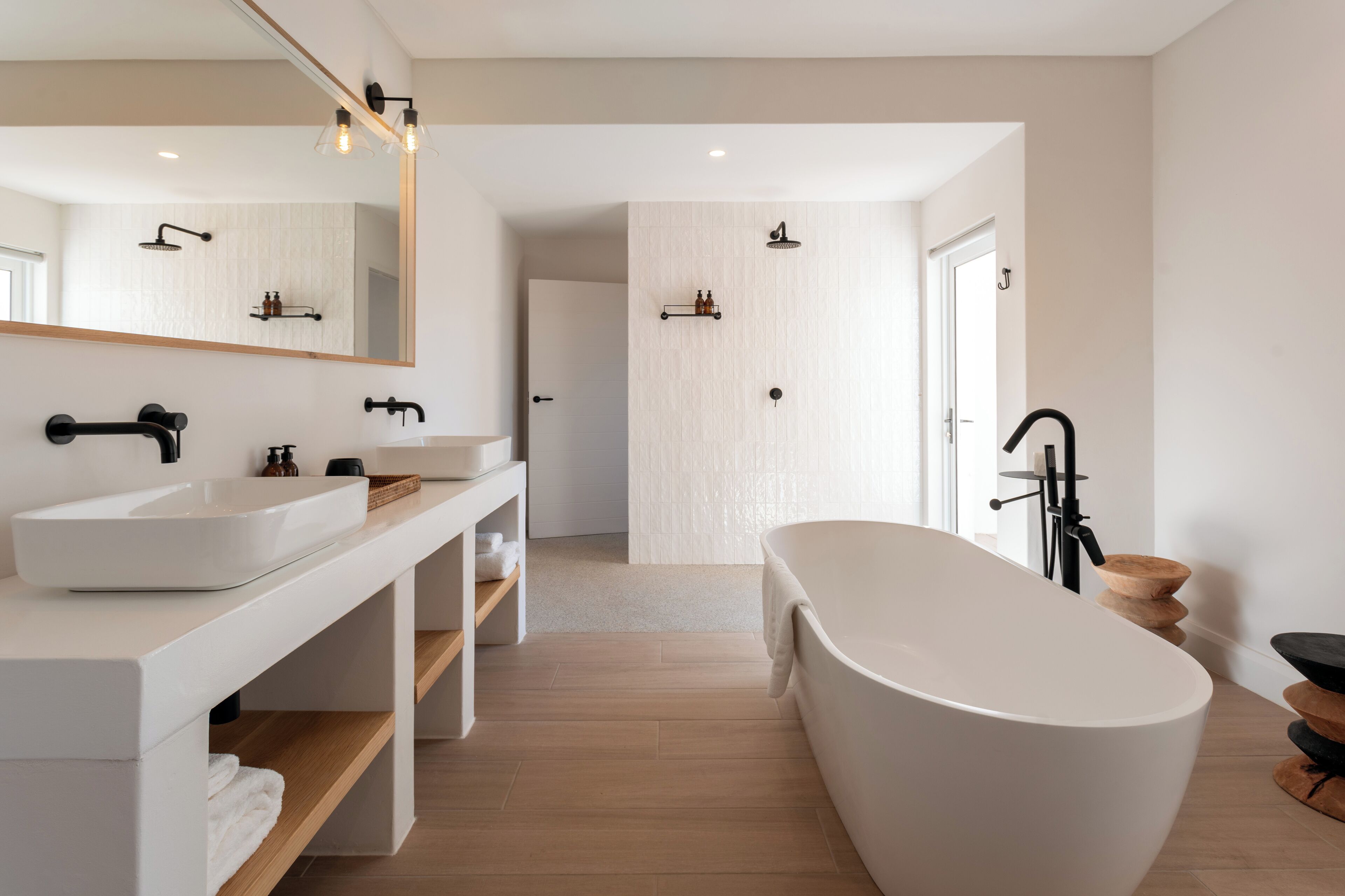 A modern bathroom with a freestanding bathtub, a large mirror, and a vanity with a sink and shelves.