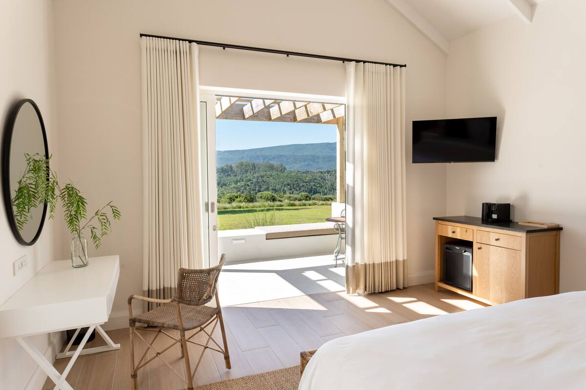 Ein Schlafzimmer mit Bett, Schreibtisch, Stuhl, Fernseher und Blick ins Freie.