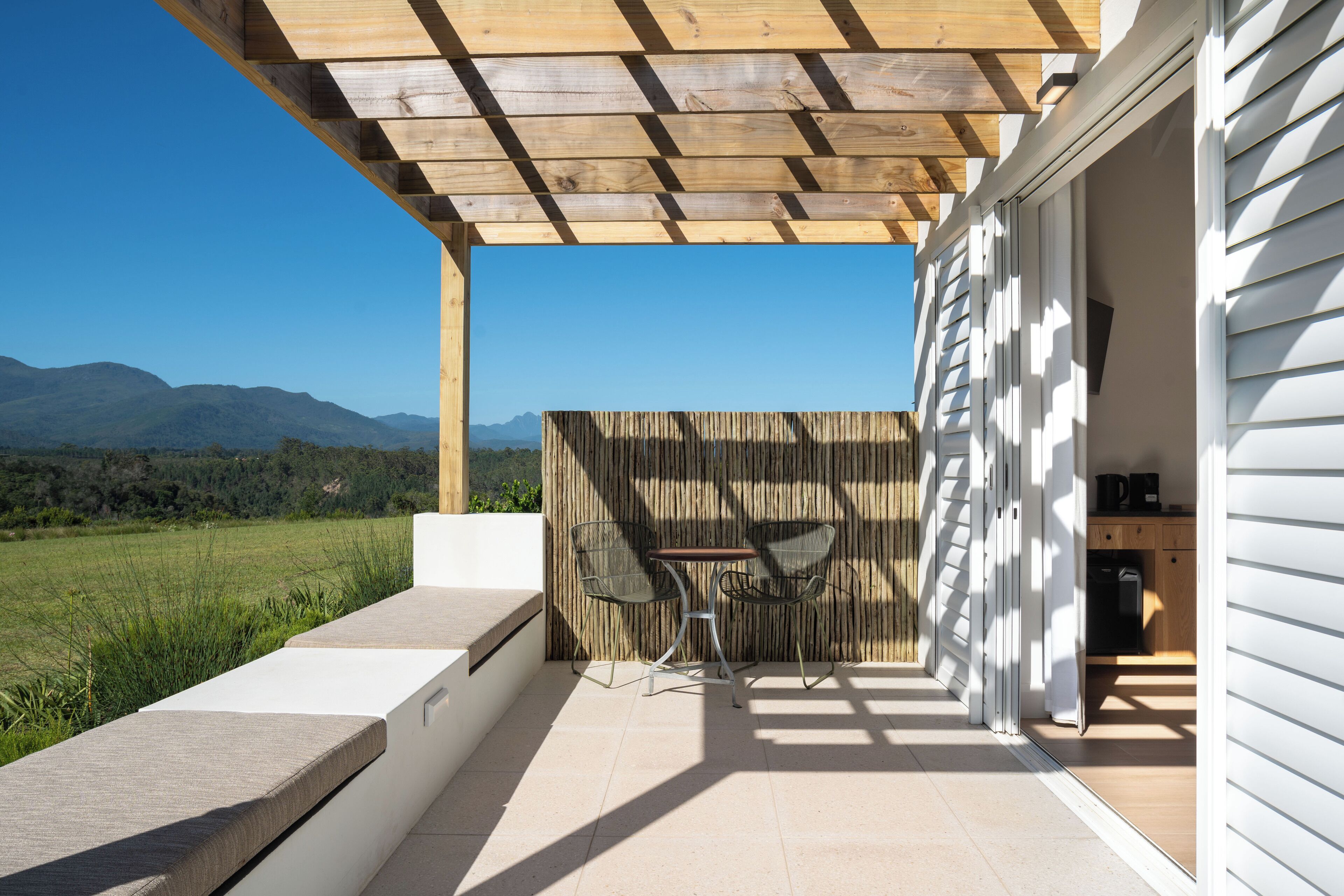 A patio with a wooden pergola, a table with chairs, and a view of mountains.