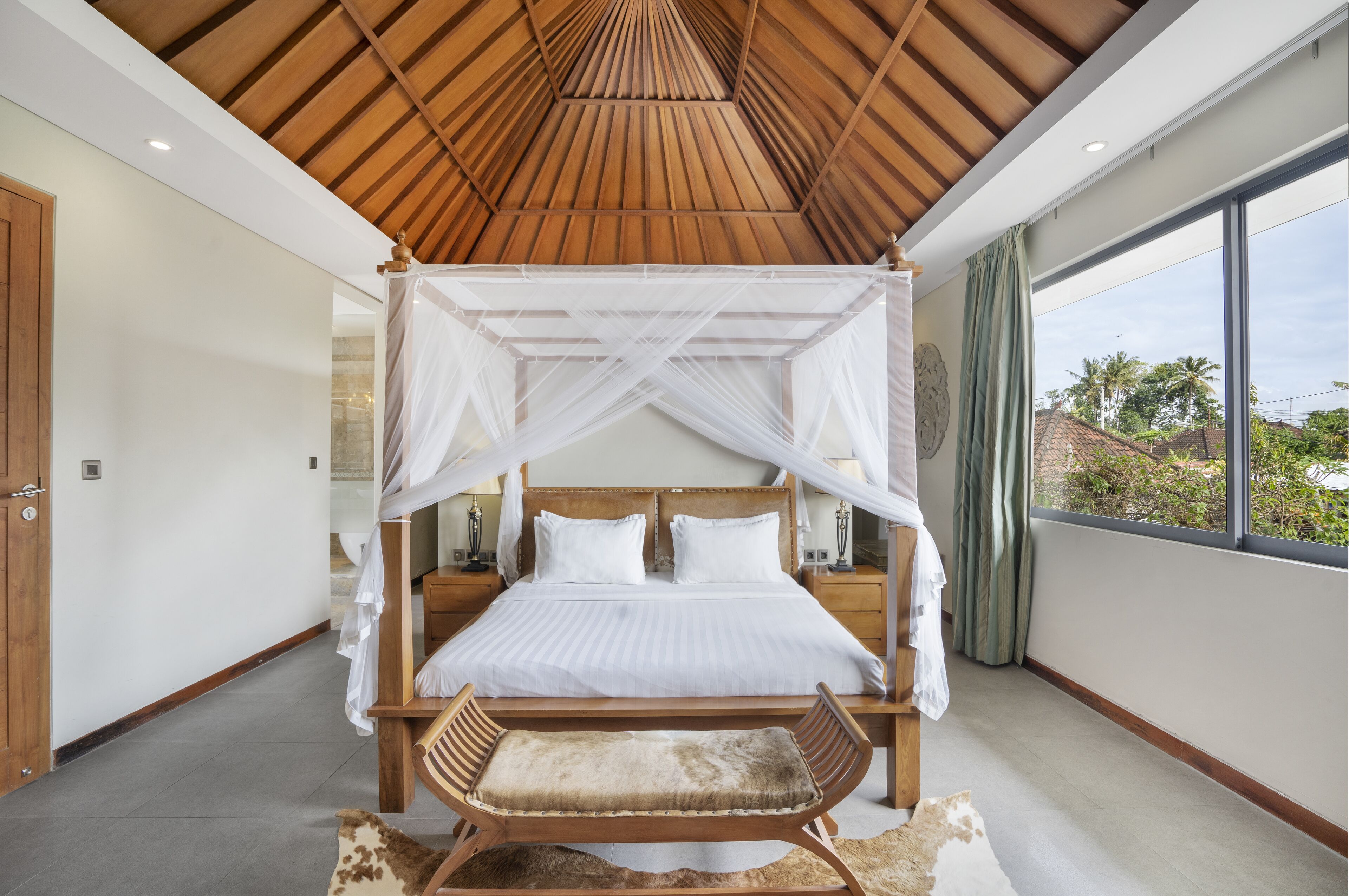 A bedroom with a canopy bed, wooden headboard, bedside tables, and a view of the outside.