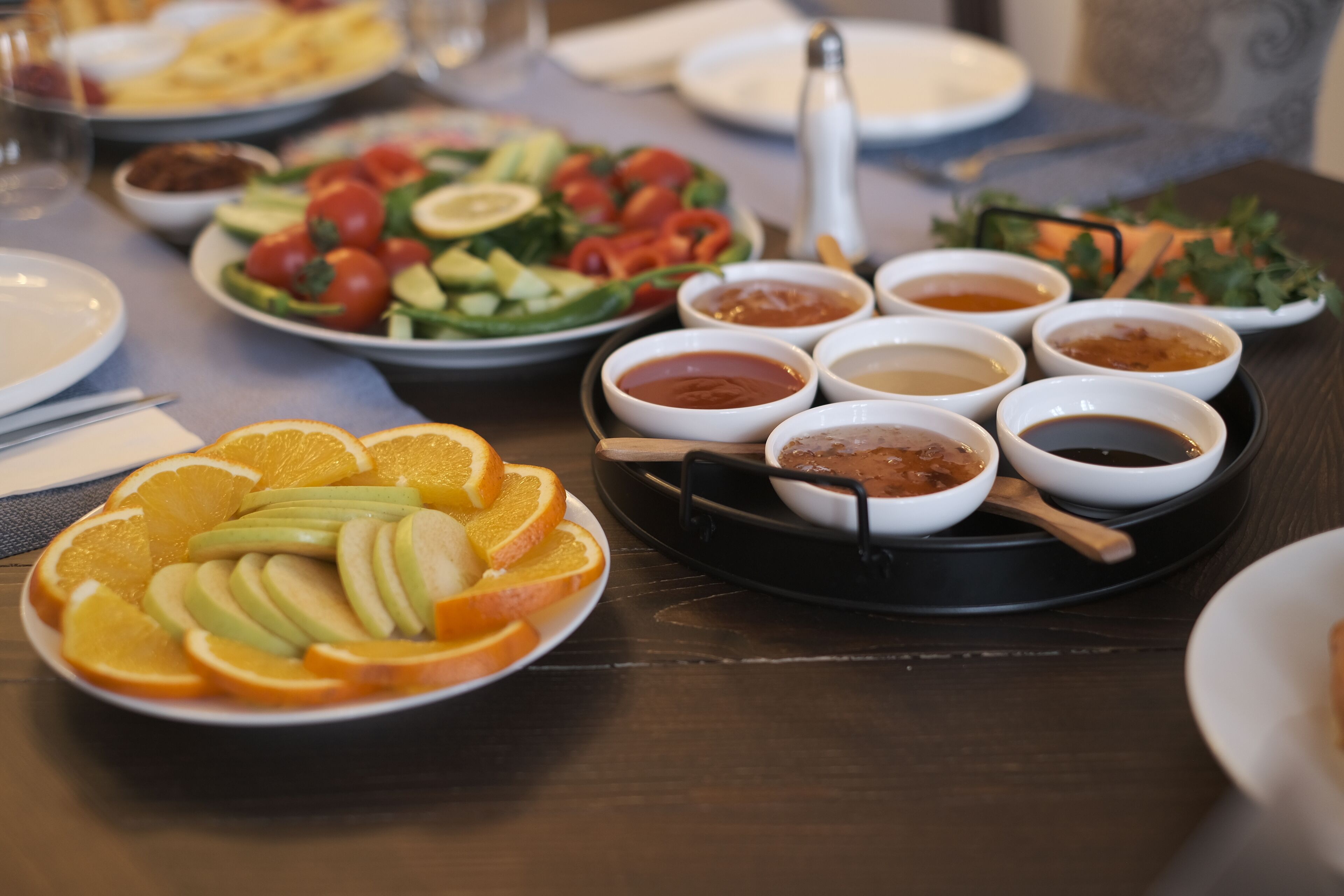 Una mesa con diversos platos, incluyendo una bandeja de frutas, ensaladas y varios recipientes pequeños con salsas.