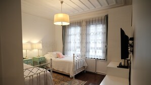 A bedroom with a bed, bedside tables, a lamp, a radiator, and a television. - Mecit Kaptan Konağı (Kastamonu)