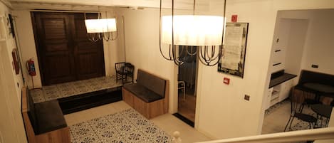 A hotel lobby with a patterned rug, a bench, a chandelier, and a wooden door.