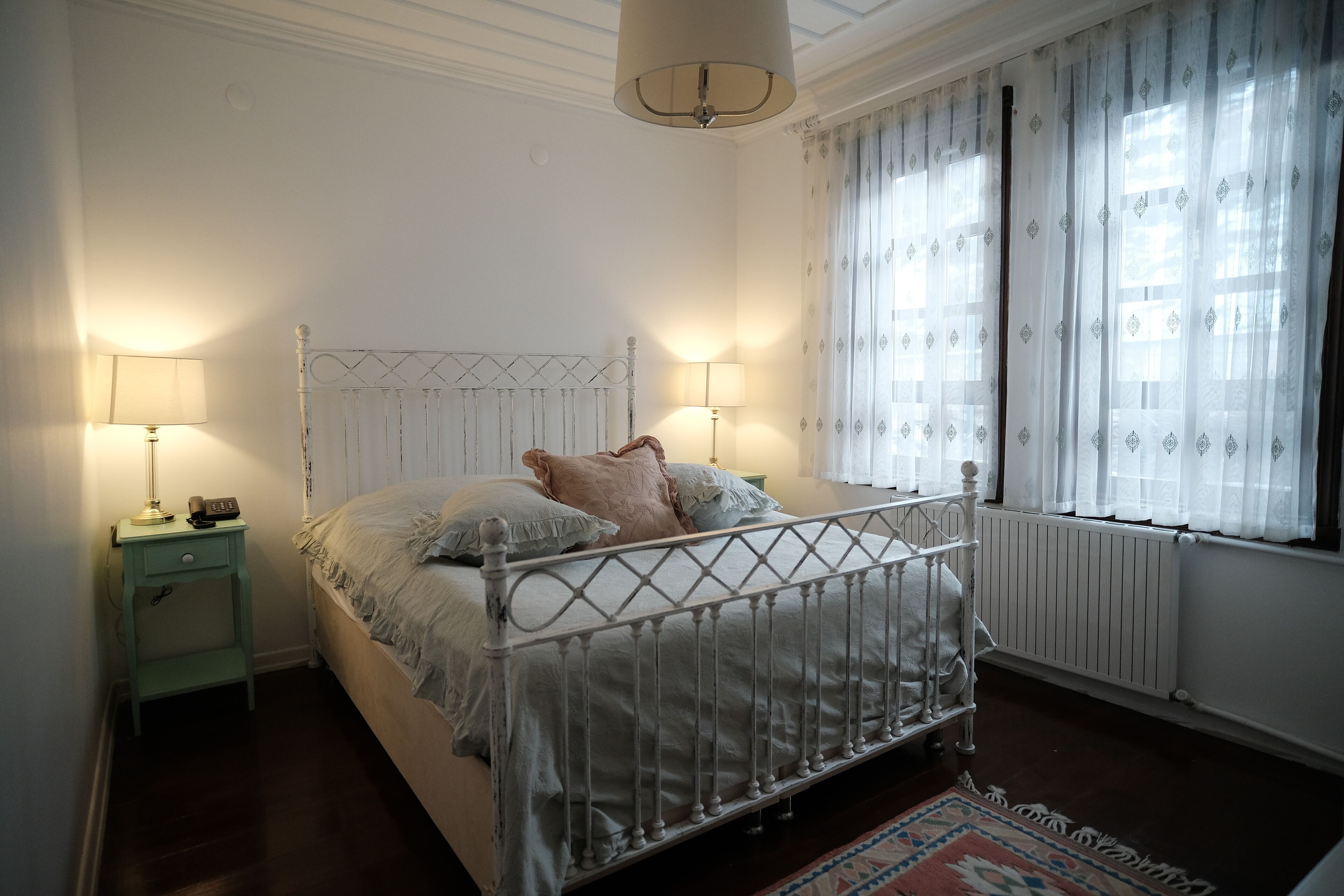 A bedroom with a bed, two bedside tables, a lamp, and a window with curtains.