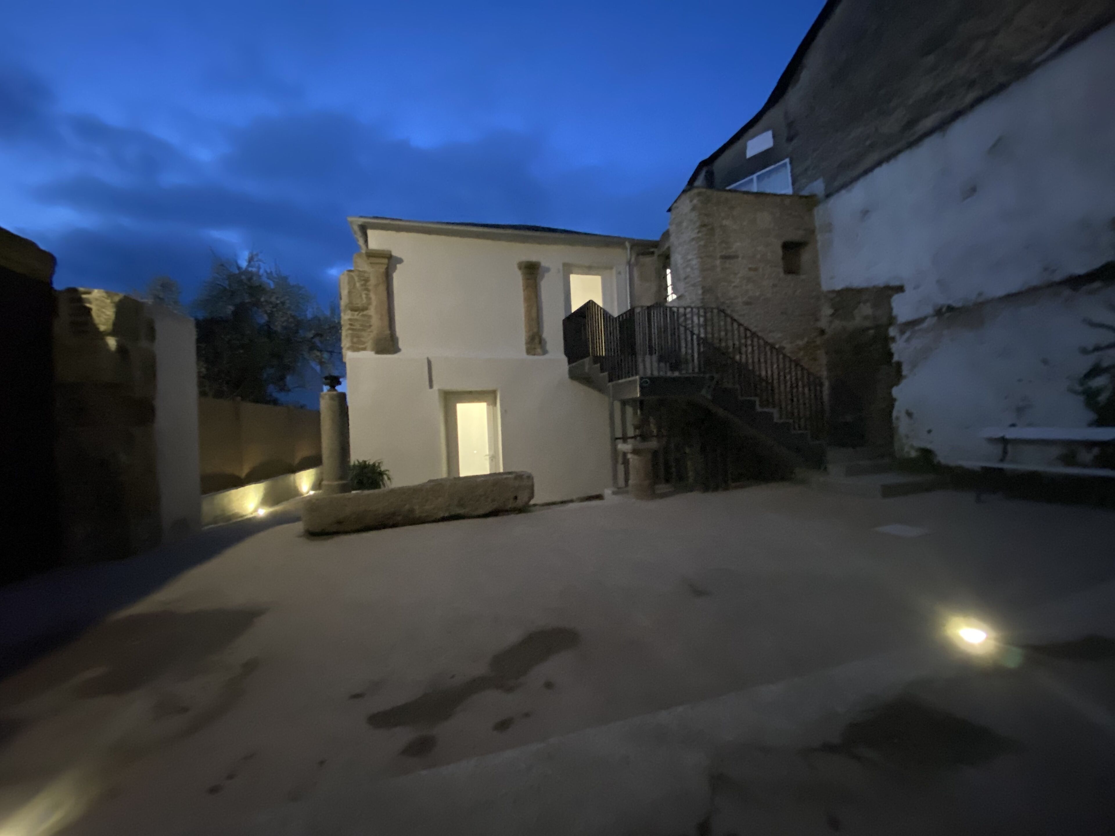 A building with a staircase leading to a door, a stone wall, and a light source near the door.