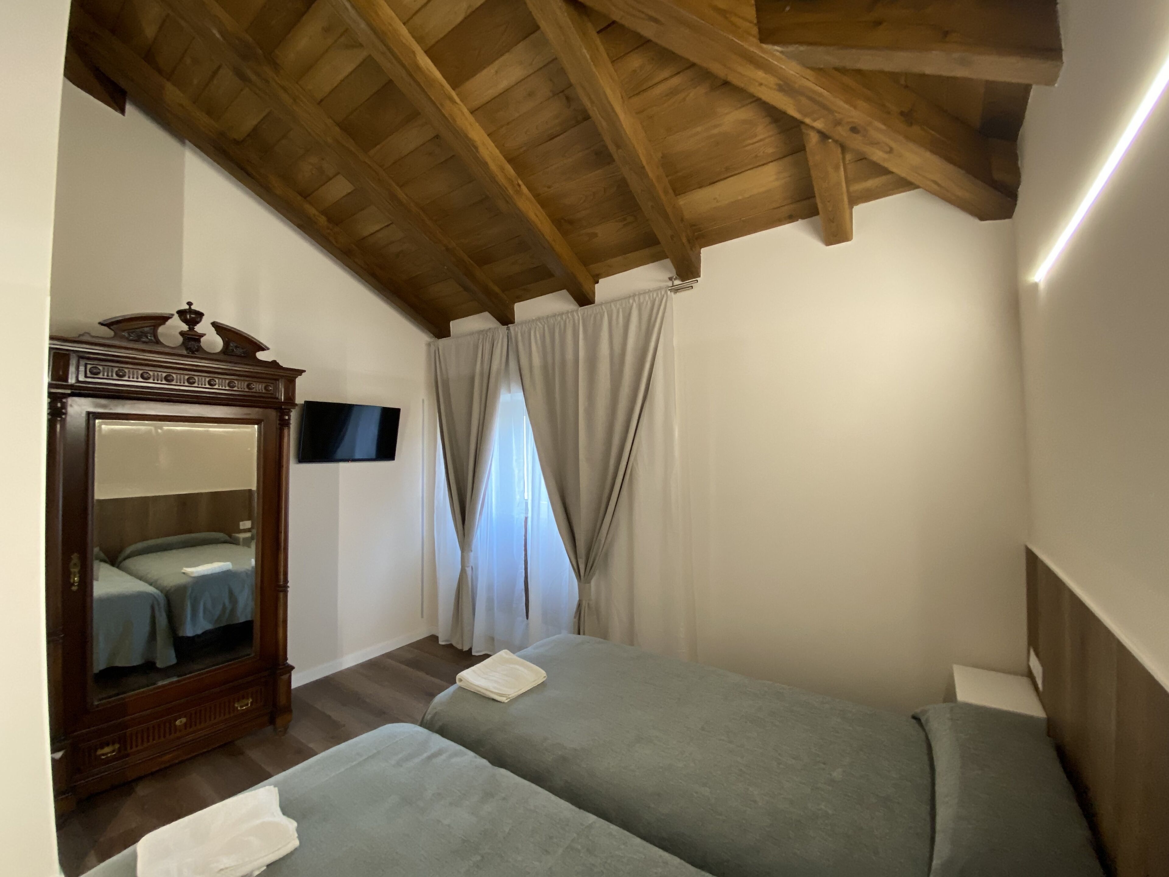 Een slaapkamer met een houten plafond, een bed met hoofdeinde, een aan de muur bevestigde televisie en een raam met gordijnen.