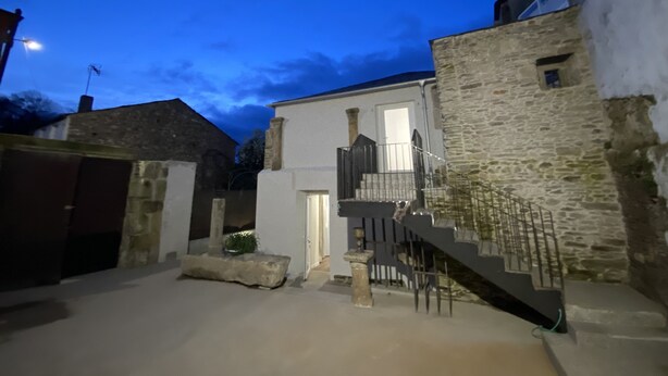 Une cour avec un bâtiment en pierre, un bâtiment blanc doté d’un balcon et un escalier.
