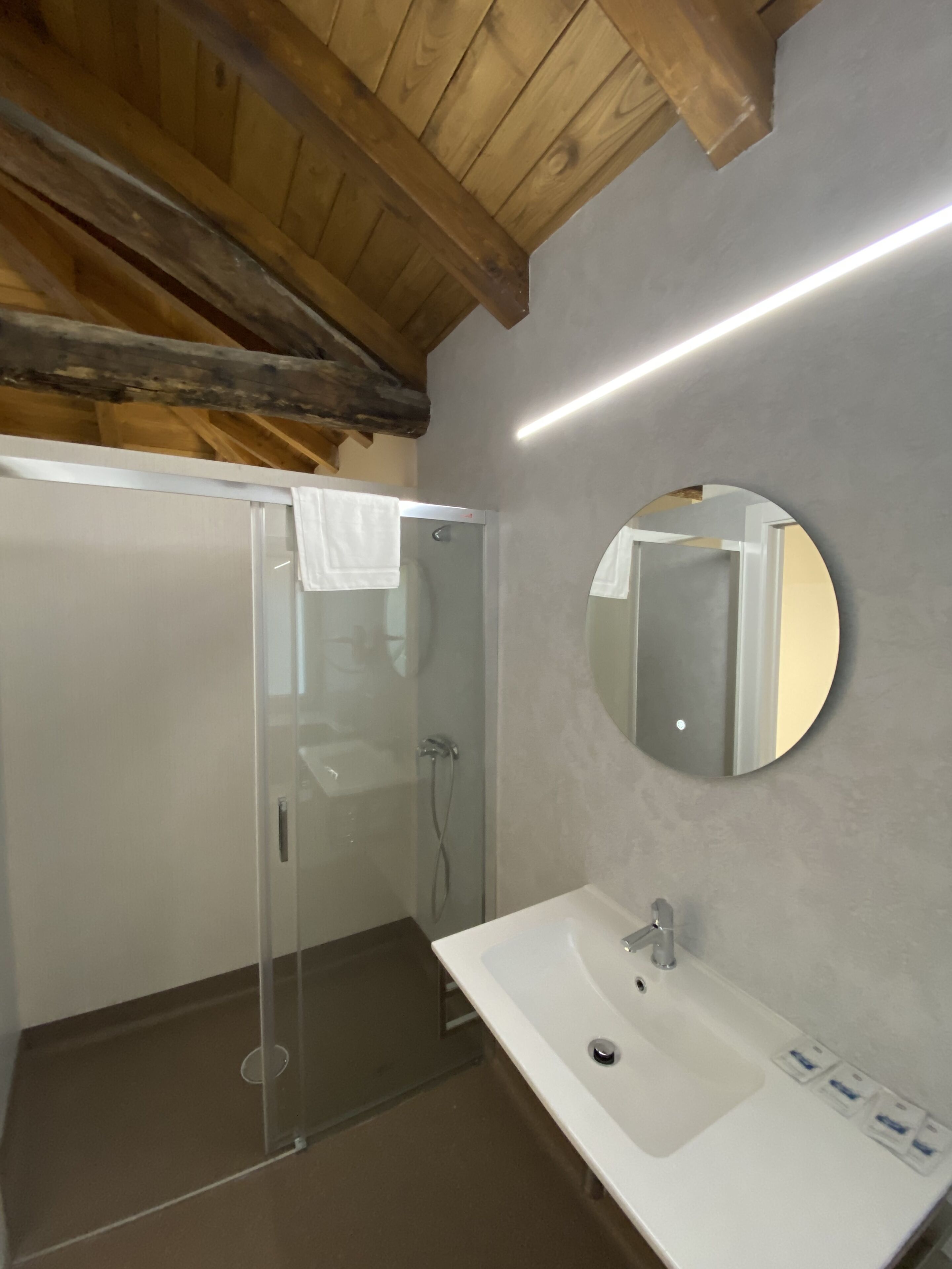 A modern bathroom with a glass-enclosed shower, a white sink, and a round mirror.