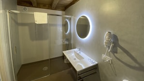 Une salle de bain moderne avec une douche à parois de verre, un lavabo blanc et un miroir doté d’un éclairage circulaire.