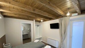 Une pièce avec des poutres en bois, un lit, une télévision, une salle de bain et une porte.