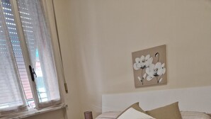 A neatly made bed with striped bedding, two pillows, and rolled towels on the floor. - Luna apartment with free parking. (nervi genova)