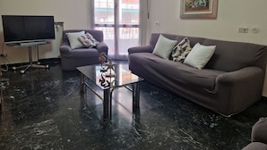 A living room with a sofa, armchair, coffee table, and a TV on a stand. - Luna apartment with free parking. (nervi genova)