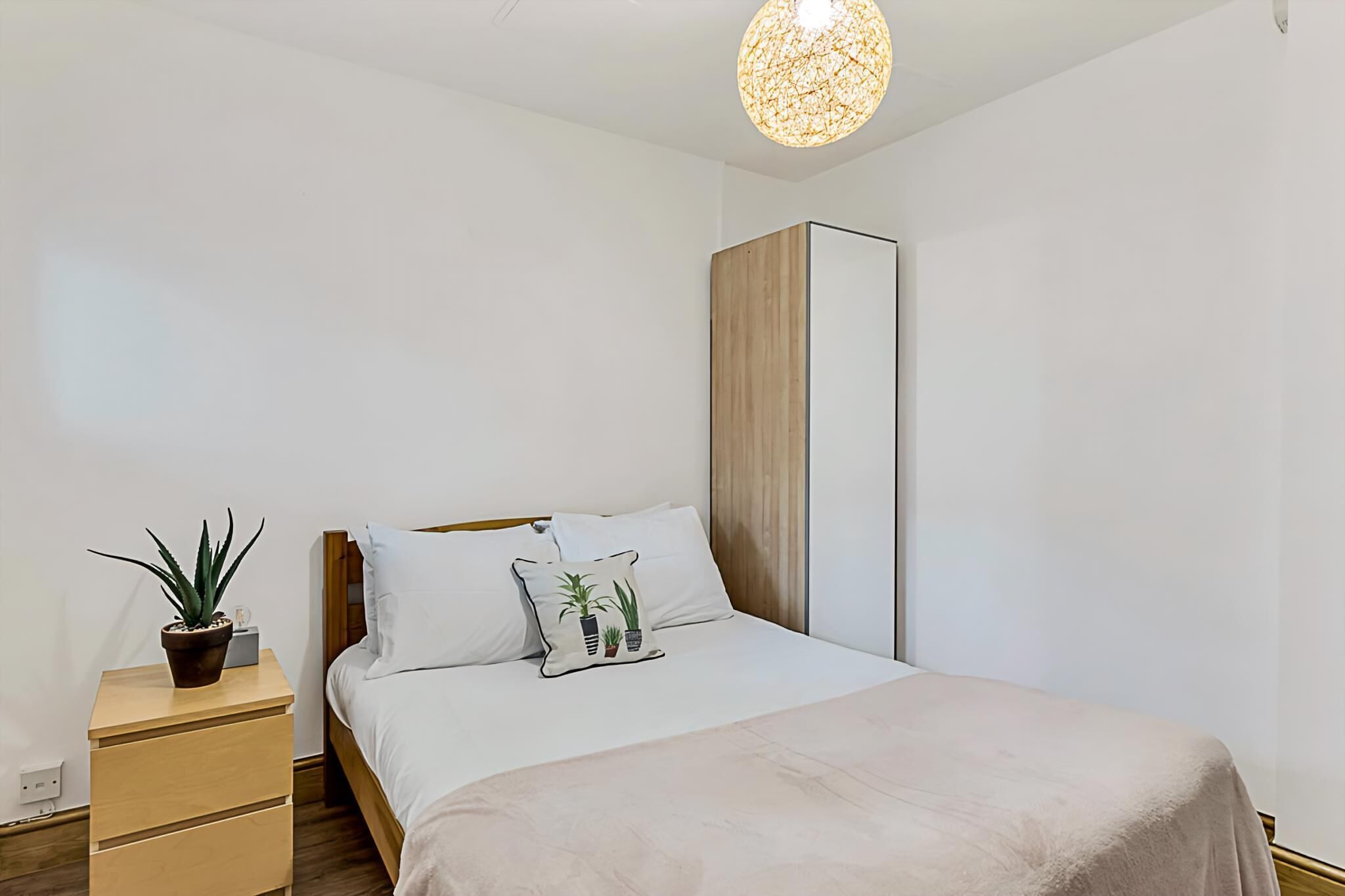 A bedroom with a bed, bedside table, potted plant, and a hanging light fixture.