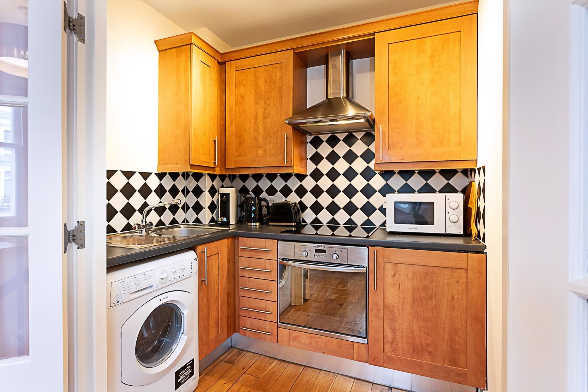 A compact kitchen with wooden cabinets, a washing machine, a microwave, and a stove.
