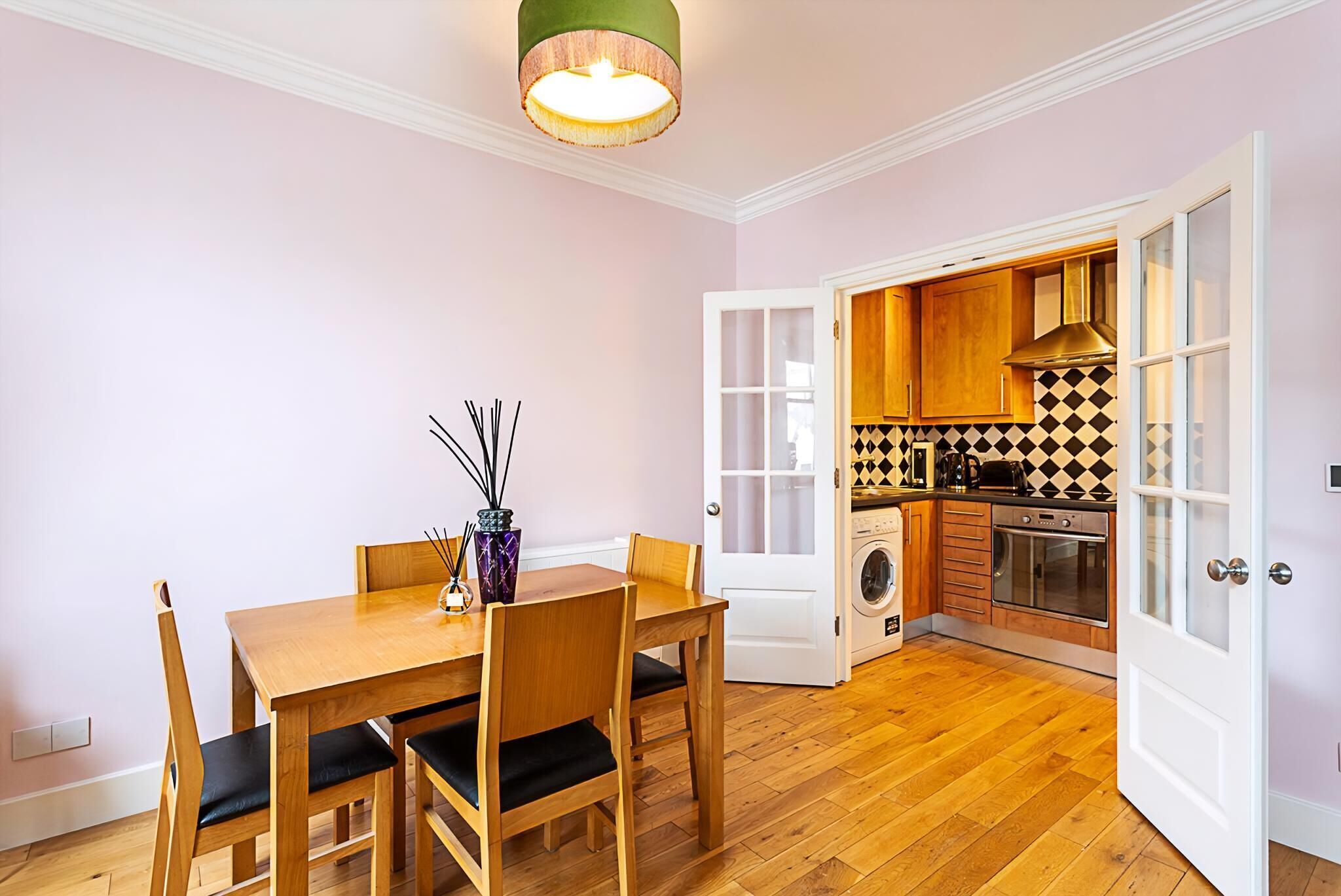 A dining area with a wooden table and chairs, a vase with sticks, and a hanging light fixture.