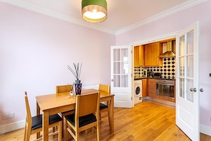 A dining area with a wooden table and chairs, a vase with sticks, and a hanging light fixture.