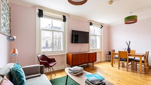 Una sala de estar moderna con sofá, mesa de centro, televisor, mesa de comedor, sillas y vistas a edificios.