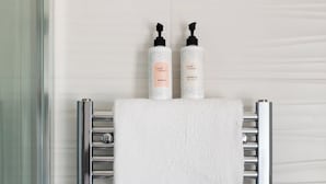 Ein Badezimmer mit einem chromfarbenen Handtuchhalter, der zwei weiße Handtücher und zwei Flaschen Shampoo und Conditioner trägt.
