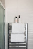 Un bagno con un portaservizi cromato che contiene due asciugamani bianchi e due flaconi di shampoo e balsamo.
