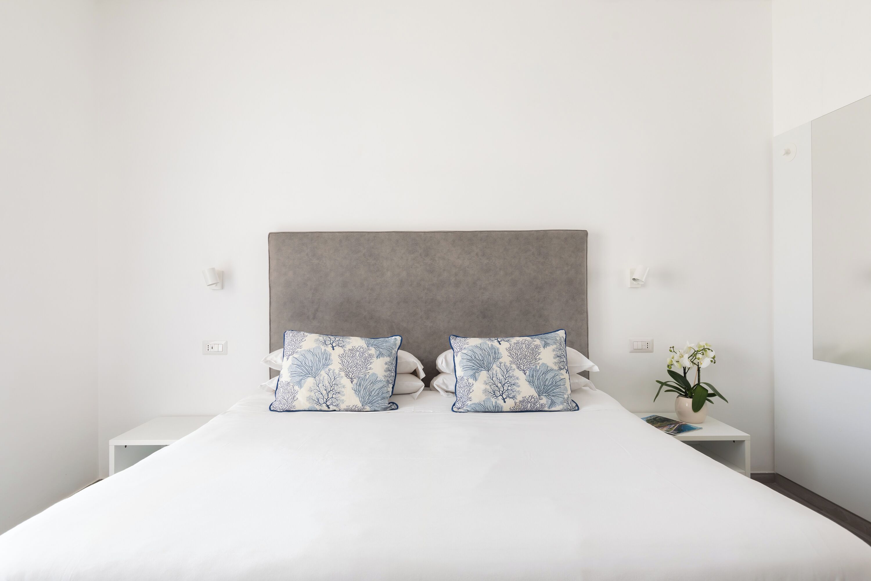 Una cama bien hecha con ropa blanca y dos almohadones decorativos de diseño azul y blanco.
