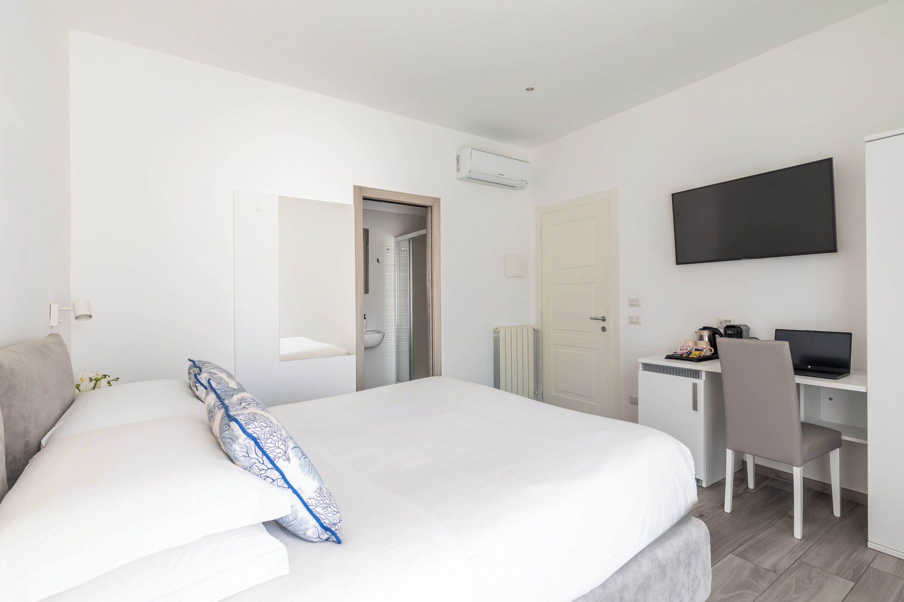 A modern hotel room with a large bed, a desk with a computer, a TV, and an air conditioning unit.