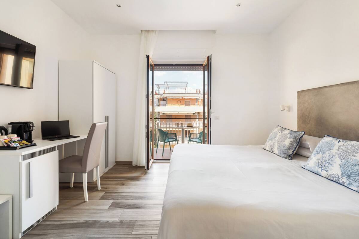 Une chambre d’hôtel avec un lit, un bureau avec un ordinateur portable, une chaise et une vue sur le balcon extérieur.