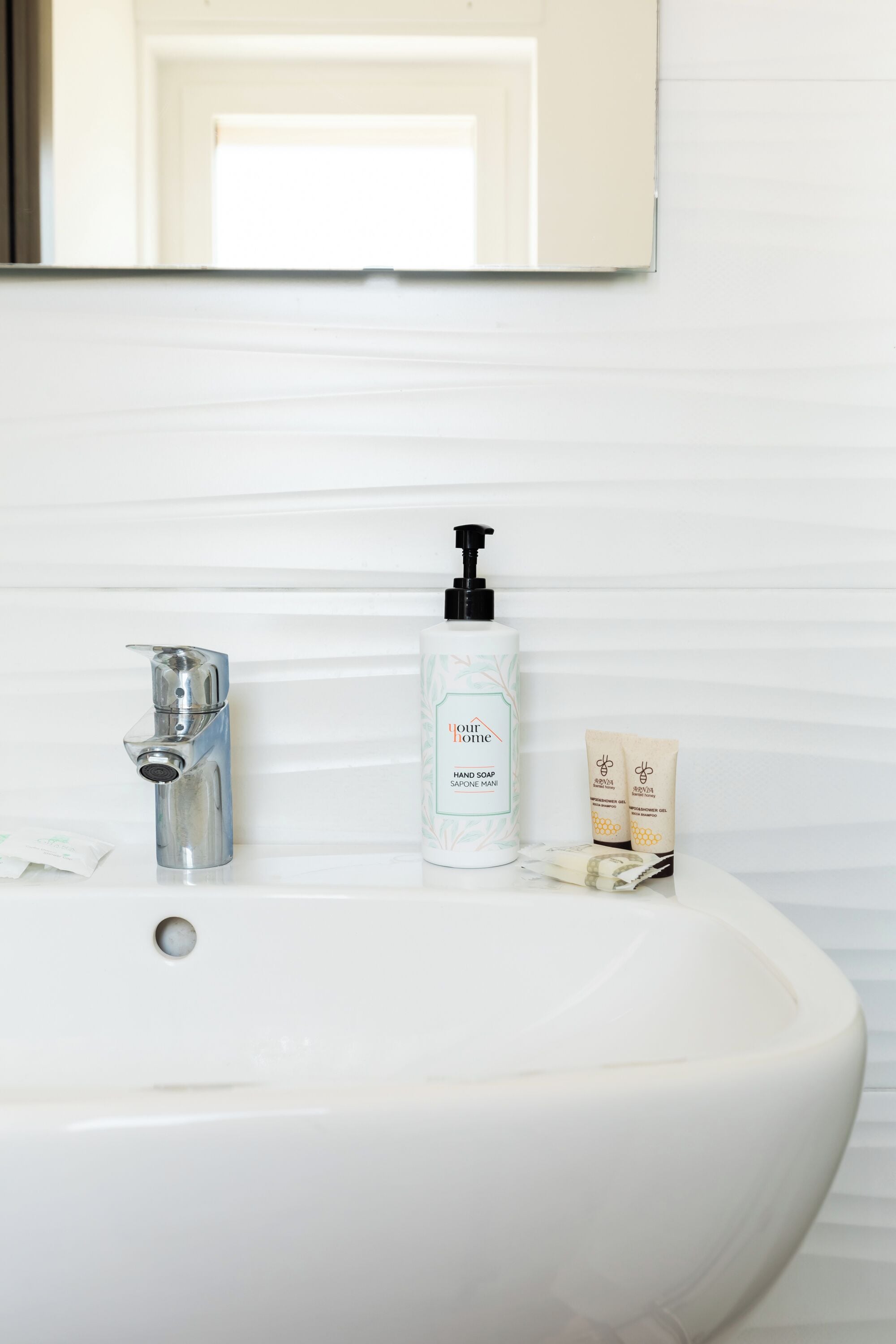 A white bathroom sink with a chrome faucet, a hand soap dispenser, and two small tubes of cream.