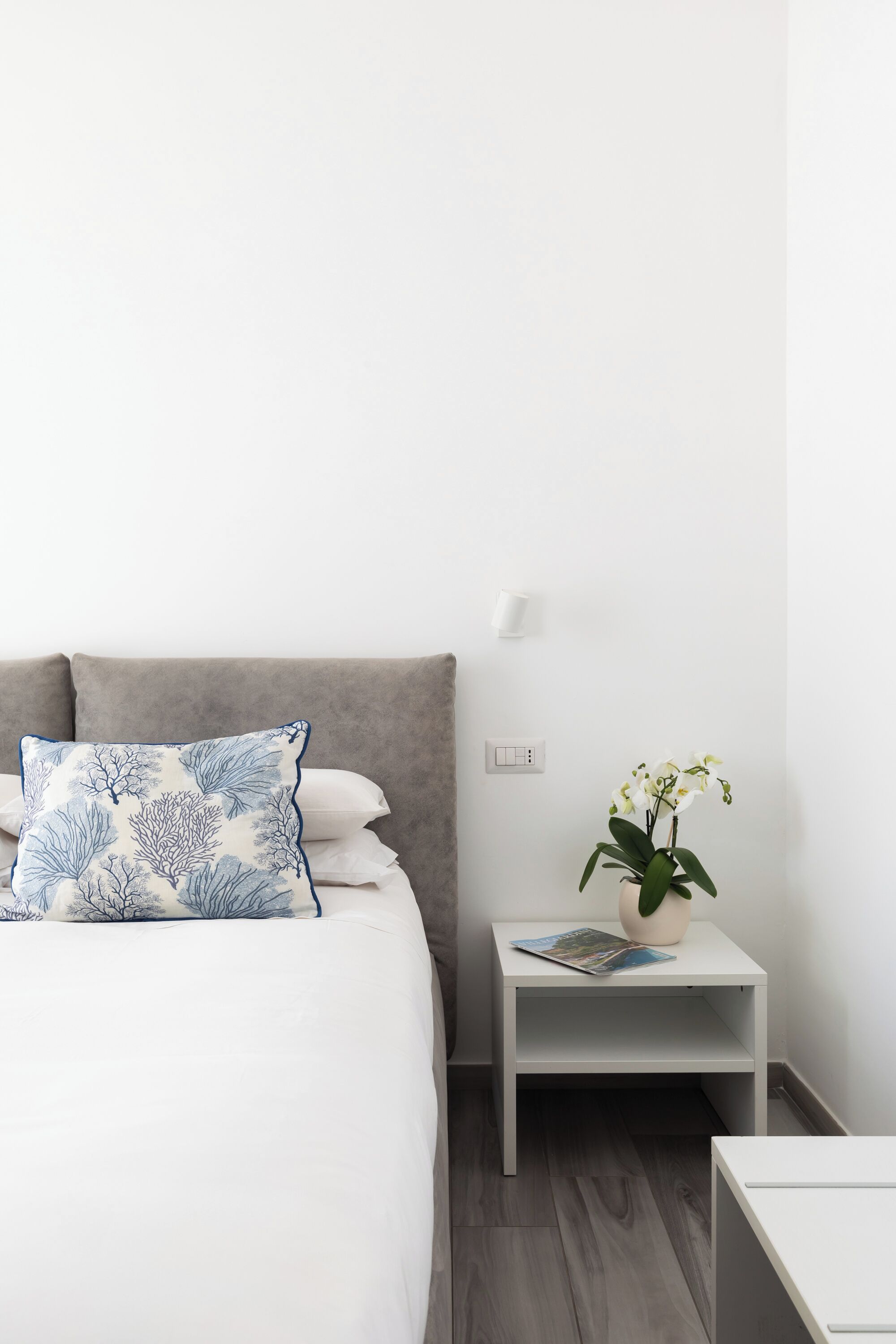 Un dormitorio ordenado con una cama, una mesita de noche con una planta y una pequeña mesa con una revista.