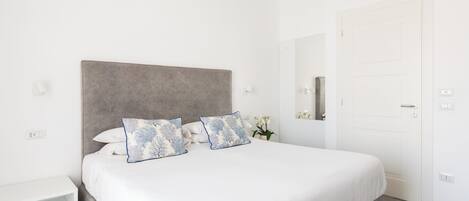 Un dormitorio ordenado con una cama grande, una mesita de noche y una puerta.