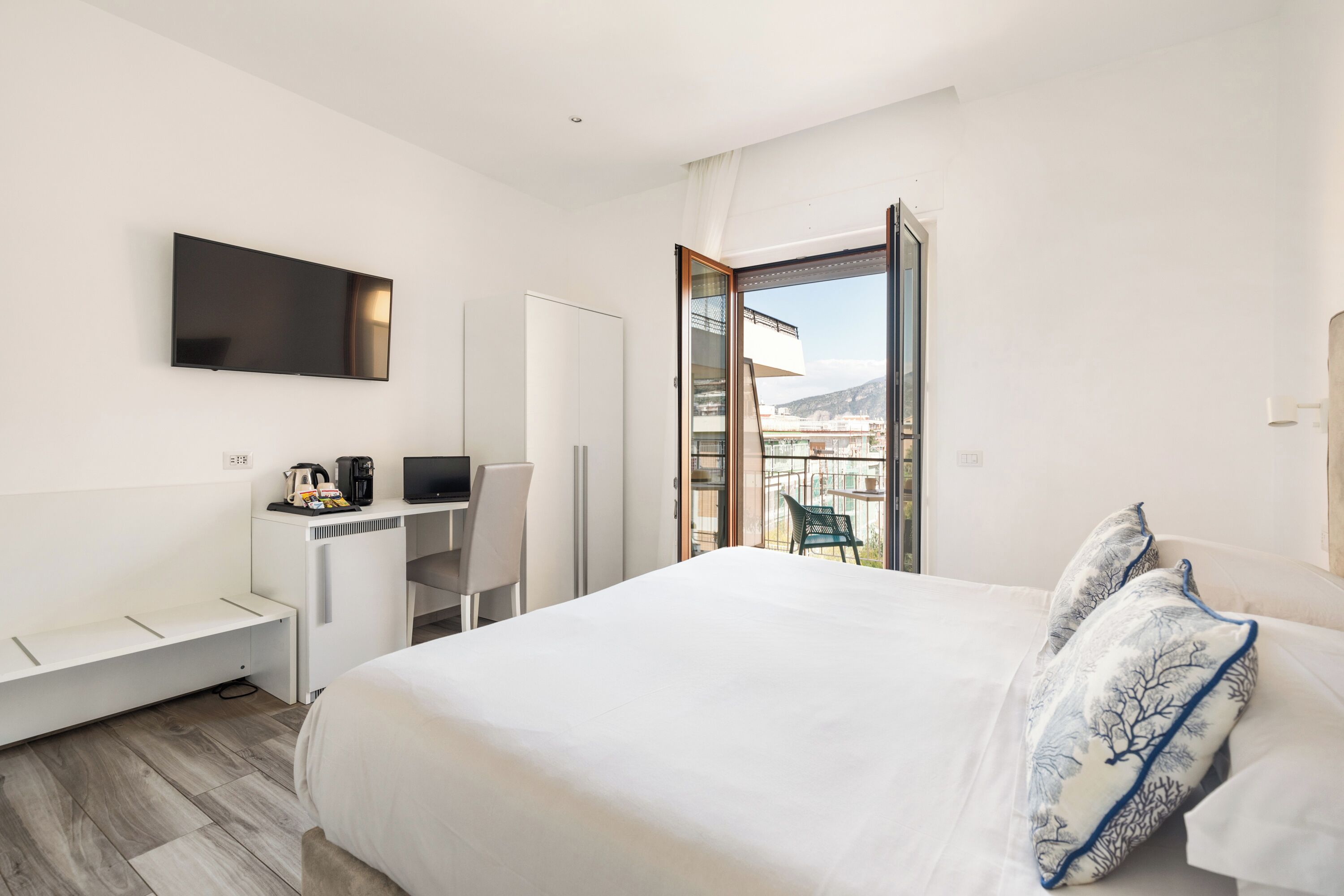A hotel room with a bed, a desk, a chair, a TV, and a balcony with a city view.