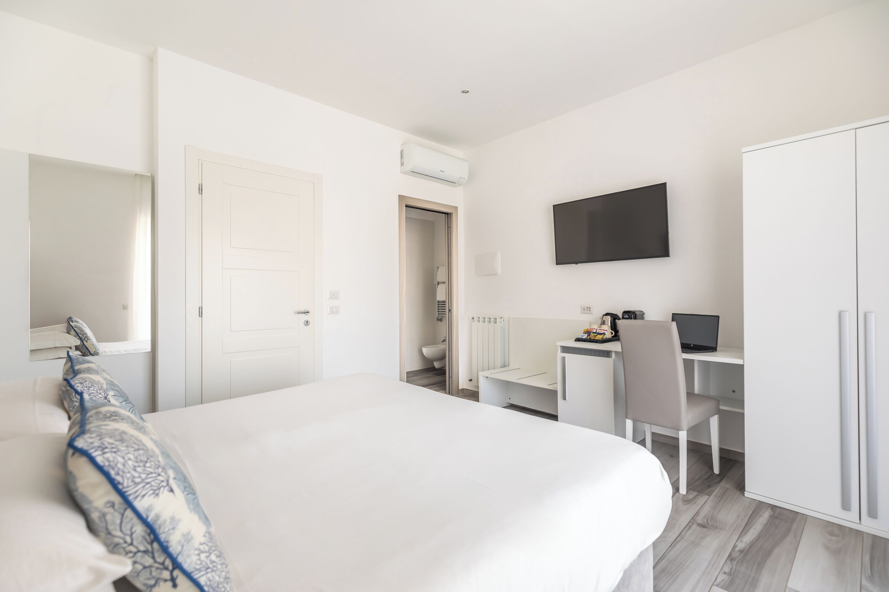 Een moderne hotelkamer met een groot bed, een bureau met een computer, een televisie en een kledingkast.