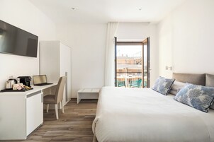 Una moderna camera d'albergo con un letto, una scrivania con un portatile, una sedia e vista sulla città attraverso un'ampia finestra.