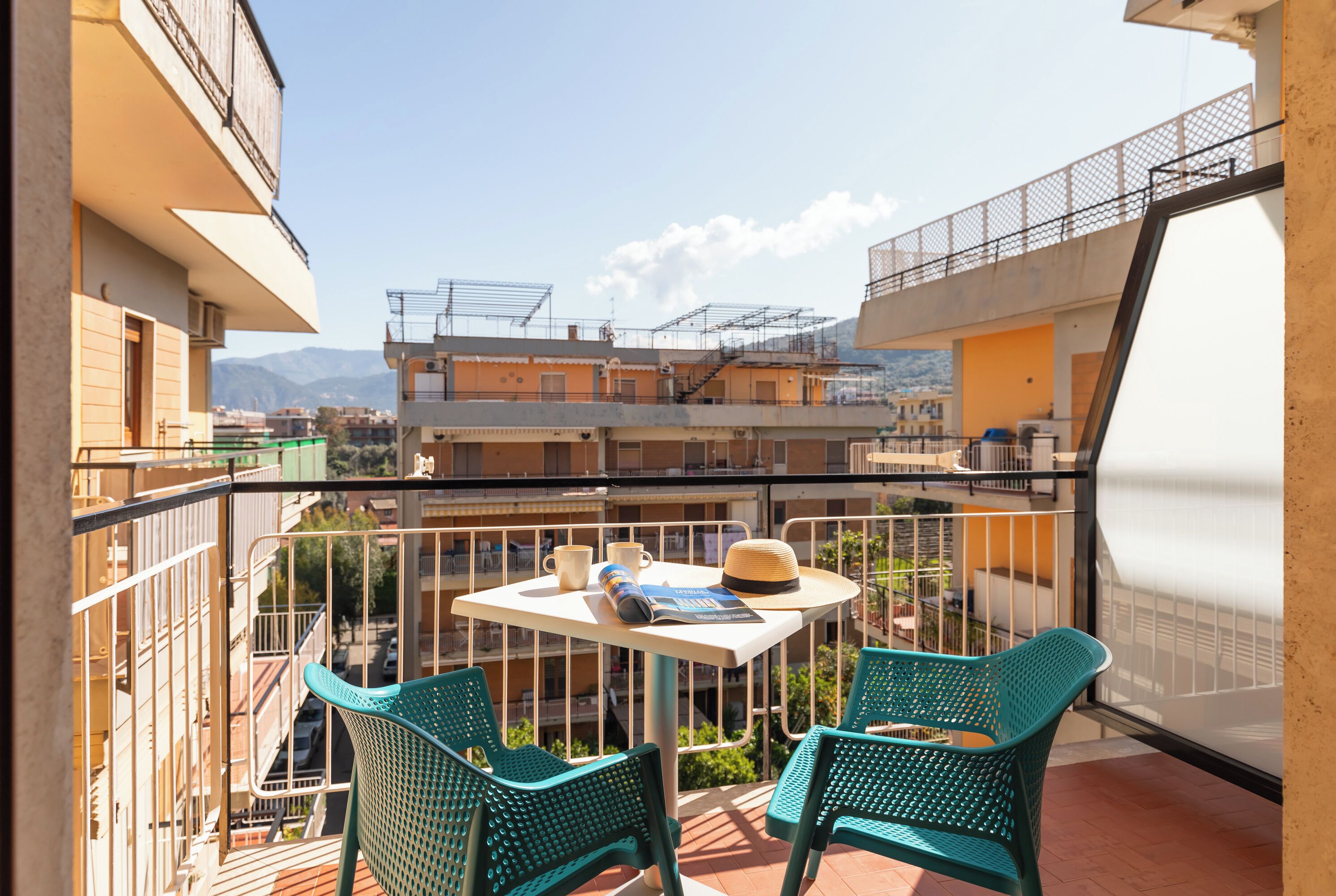 Ein Balkon mit zwei grünen Stühlen, einem kleinen Tisch und einem Hut.