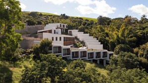 A modern multi-story building with a unique stepped design, surrounded by lush greenery and hills. - PAPANGUE Hôtel & Spa (L'Étang-Salé)