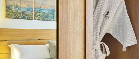 Habitación de hotel con cama de madera, ropa de cama blanca, cabecero de madera y un cuadro de palmeras en la pared.