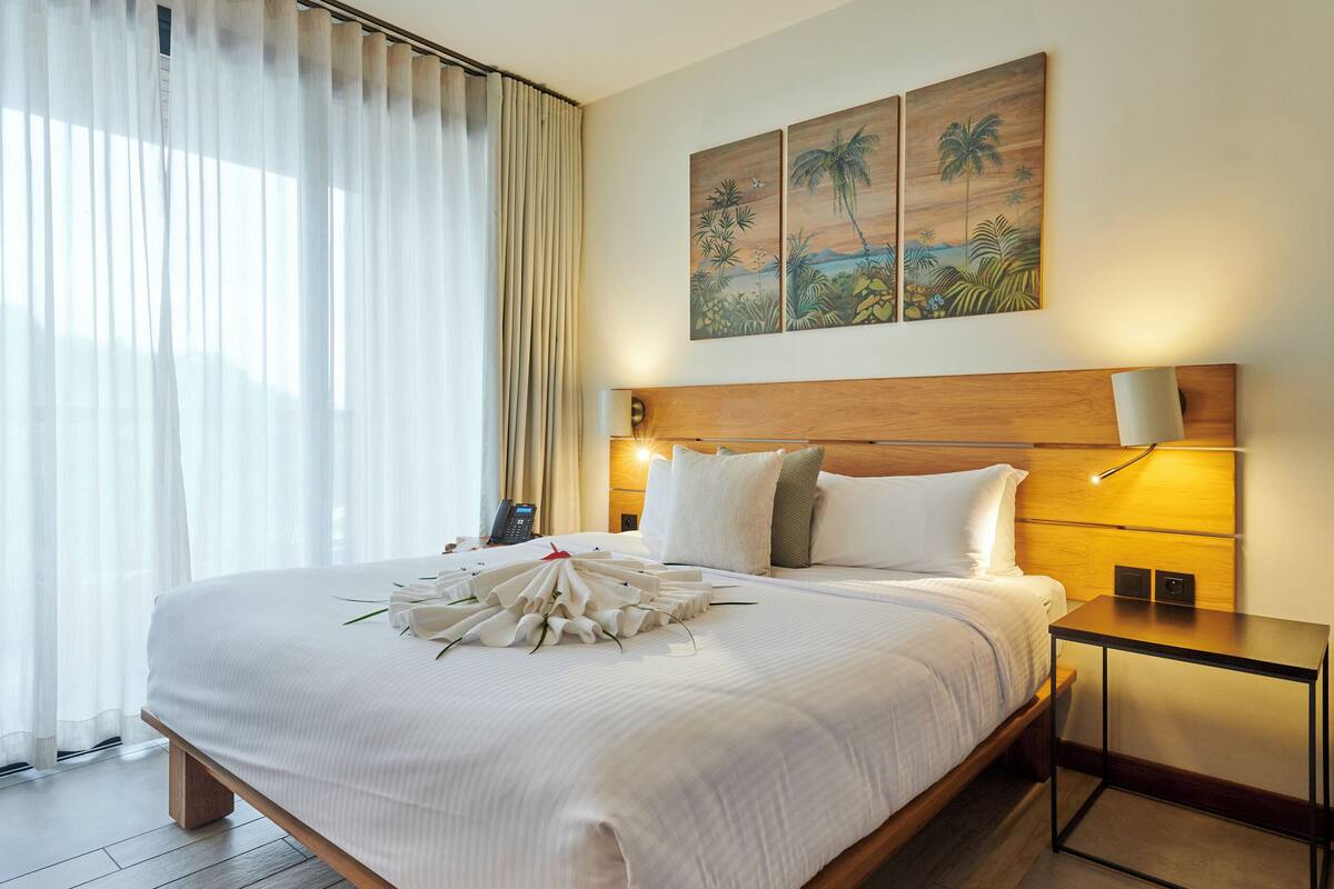 A spacious bedroom with a large bed, a ceiling fan, a bedside table with a lamp, and a painting on the wall.