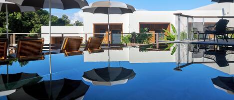 A poolside area with umbrellas, lounge chairs, and a modern building with large windows.