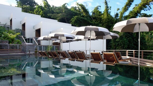 A pool area with lounge chairs and umbrellas, surrounded by a white building and lush greenery. - PAPANGUE Hôtel & Spa (L'Étang-Salé)