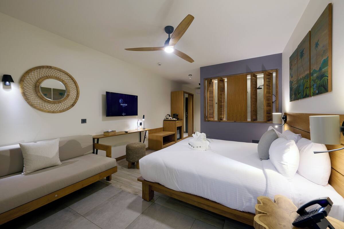 A modern hotel room with a bed, a sofa, a desk, and a TV.