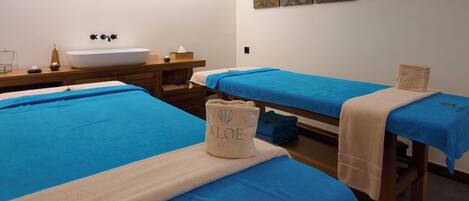A spa room with two beds, a sink, and a wooden table.